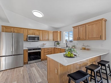 Kitchen featuring appliances with stainless steel finishes, a kitchen breakfast bar, light wood-type flooring, vaulted ceiling, and a peninsula