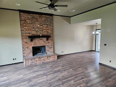 Unfurnished living room featuring ceiling fan, crown molding, wood finished floors, a chandelier, and a brick fireplace
