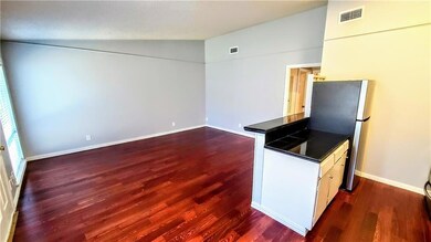Kitchen with dark wood-style flooring, open floor plan, dark countertops, freestanding refrigerator, and lofted ceiling