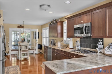 Kitchen featuring appliances with stainless steel finishes, recessed lighting, decorative light fixtures, light stone countertops, and light wood-style floors
