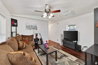 Living area featuring dark wood-style flooring, a ceiling fan, lofted ceiling, and ornamental molding