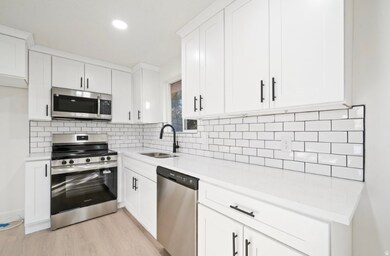 Kitchen featuring stainless steel appliances, white cabinetry, light wood-type flooring, light stone counters, and recessed lighting