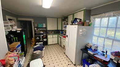 Kitchen featuring white refrigerator with ice dispenser, crown molding, light flooring, green cabinetry, and stainless steel microwave
