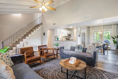 Living room featuring wood finished floors, stairs, a ceiling fan, beam ceiling, and a towering ceiling