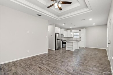 Unfurnished living room featuring a tray ceiling, a ceiling fan, wood finished floors, baseboards, and visible vents