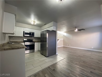 Kitchen featuring appliances with stainless steel finishes, light wood-type flooring, dark countertops, white cabinets, and ceiling fan