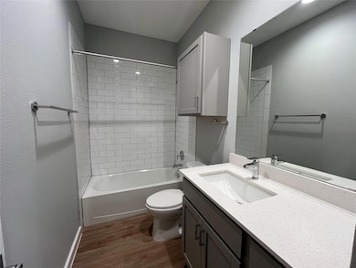 Bathroom featuring dark wood-style floors, vanity, washtub / shower combination, and a textured wall