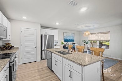 Kitchen with appliances with stainless steel finishes, white cabinetry, light wood finished floors, a kitchen island with sink, and light stone counters