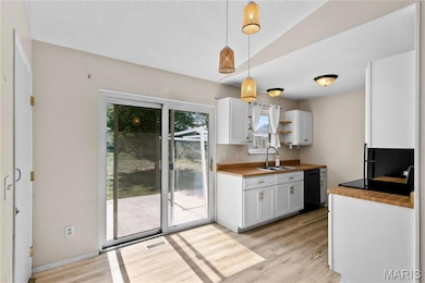 Kitchen with white cabinets, light wood-style flooring, a textured ceiling, pendant lighting, and wooden counters