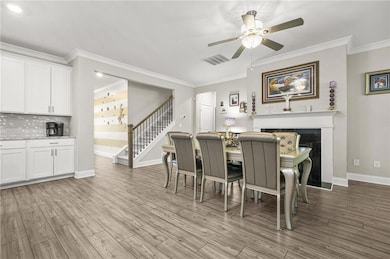 Dining room with crown molding, stairway, light wood finished floors, a fireplace, and ceiling fan