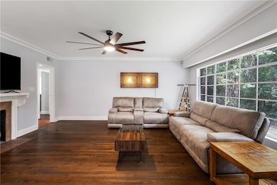Living area with crown molding, wood finished floors, ceiling fan, and a fireplace with flush hearth