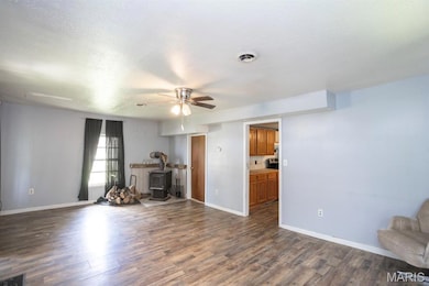 Unfurnished living room featuring a wood stove, ceiling fan, dark wood-style floors, and a textured ceiling