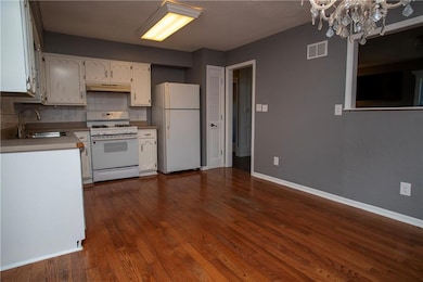Kitchen with white appliances, under cabinet range hood, a chandelier, white cabinets, and dark wood finished floors