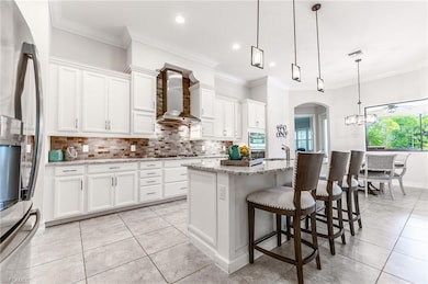 Kitchen featuring appliances with stainless steel finishes, wall chimney exhaust hood, backsplash, white cabinetry, and ornamental molding