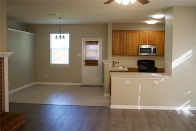Kitchen featuring electric range, light countertops, brown cabinets, stainless steel microwave, and light tile patterned floors