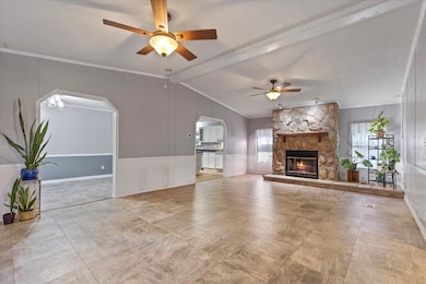 Unfurnished living room with a ceiling fan, lofted ceiling, ornamental molding, a stone fireplace, and arched walkways