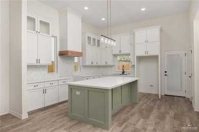 Kitchen featuring pendant lighting, white cabinets, sink, light wood-type flooring, and a kitchen island