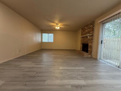 Unfurnished living room featuring a textured ceiling, light wood-style flooring, a brick fireplace, a textured wall, and a ceiling fan