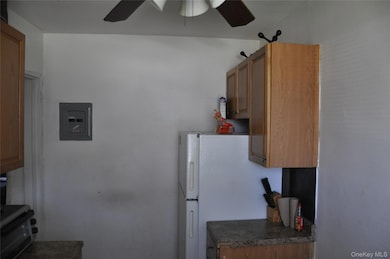 Kitchen with a ceiling fan, electric panel, dark countertops, brown cabinets, and freestanding refrigerator