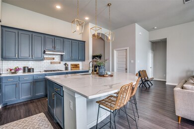 Kitchen featuring a  breakfast bar, dark wood-type flooring, backsplash, a center island with sink, and light stone counters