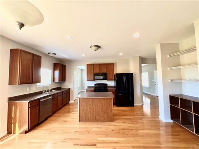 Kitchen featuring light wood-type flooring, a center island, dark countertops, and black appliances