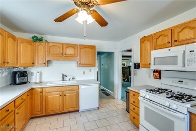 Kitchen featuring light tile patterned floors, white appliances, sink, and ceiling fan