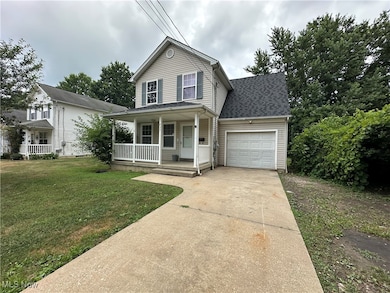 Traditional home with a porch, an attached garage, concrete driveway, a shingled roof, and a front lawn