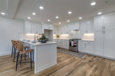 Kitchen featuring stainless steel stove, white cabinets, recessed lighting, premium range hood, and light wood-style floors