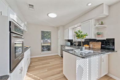 Kitchen with dark stone counters, white cabinetry, decorative backsplash, light wood-style floors, and open shelves