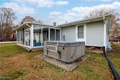 Rear view of property featuring a sunroom, a chimney, a yard, and a hot tub