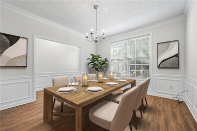 Dining space with a chandelier, dark wood-style flooring, ornamental molding, a wainscoted wall, and a textured ceiling