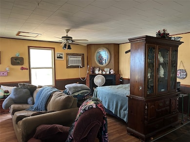 Bedroom featuring wooden walls, wainscoting, wood finished floors, a ceiling fan, and a wall unit AC