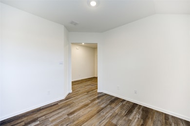 This photo showcases a bright, empty room with white walls and wood-style flooring, leading into another area through an open doorway.