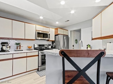 Kitchen with white cabinets, appliances with stainless steel finishes, recessed lighting, backsplash, and brown cabinets