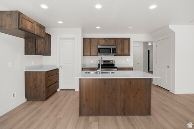 Kitchen featuring recessed lighting, stainless steel appliances, light wood-style floors, a kitchen island with sink, and light stone countertops