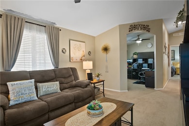 Living area with a ceiling fan, carpet floors, vaulted ceiling, and an office area