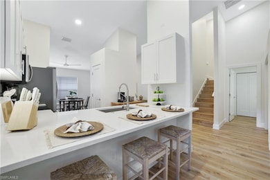 Kitchen featuring a sink, a kitchen breakfast bar, white cabinets, a peninsula, and light wood-type flooring