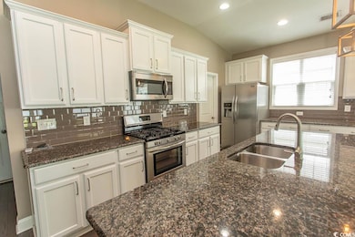 Kitchen featuring appliances with stainless steel finishes, white cabinetry, decorative backsplash, vaulted ceiling, and dark stone counters