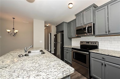Kitchen with appliances with stainless steel finishes, gray cabinets, a chandelier, and tasteful backsplash