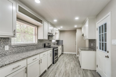 Kitchen featuring light stone countertops, stainless steel appliances, white cabinetry, decorative backsplash, and recessed lighting