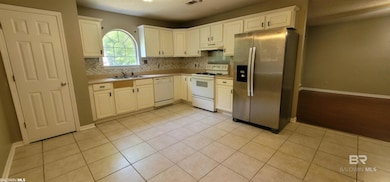 Kitchen with white appliances, decorative backsplash, light countertops, light tile patterned floors, and under cabinet range hood