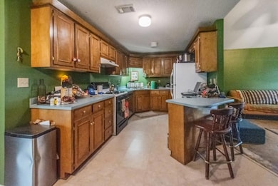 Kitchen with brown cabinetry, white appliances, a kitchen bar, light countertops, and a textured ceiling
