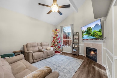 Living room with a tiled fireplace, wood finished floors, high vaulted ceiling, beamed ceiling, and ceiling fan