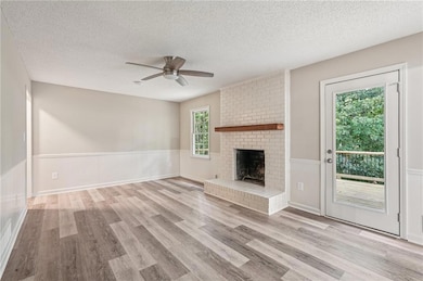 Unfurnished living room with ceiling fan, wood finished floors, a textured ceiling, wainscoting, and a brick fireplace
