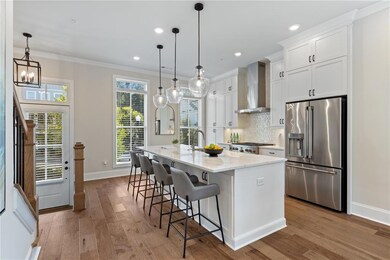 Kitchen featuring high quality fridge, wall chimney range hood, a kitchen island with sink, crown molding, and light wood-type flooring