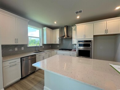 Kitchen with wall chimney range hood, stainless steel appliances, a sink, light wood-type flooring, and white cabinets