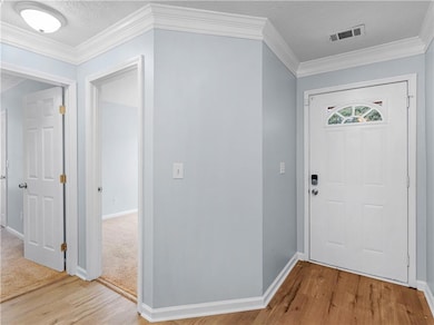 Entrance foyer with a textured ceiling, crown molding, and light wood-type flooring