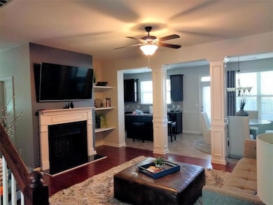 Living room with decorative columns, hardwood / wood-style flooring, and ceiling fan with notable chandelier