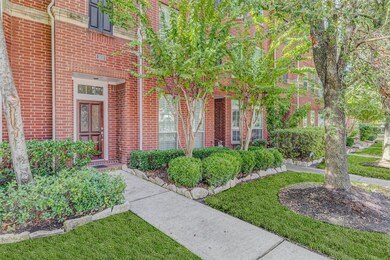 A private pathway framed by lush, professionally maintained hedges and stone-edged flowerbeds leads to the stately front door. Mature crepe myrtles and manicured greenery line the sidewalk, offering shade, privacy, and beautiful curb appeal that complements the home’s striking red brick facade in this peaceful, tree-lined section of Rice Military.