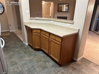 Kitchen featuring brown cabinetry, light countertops, a fireplace, and dark stone finish floors